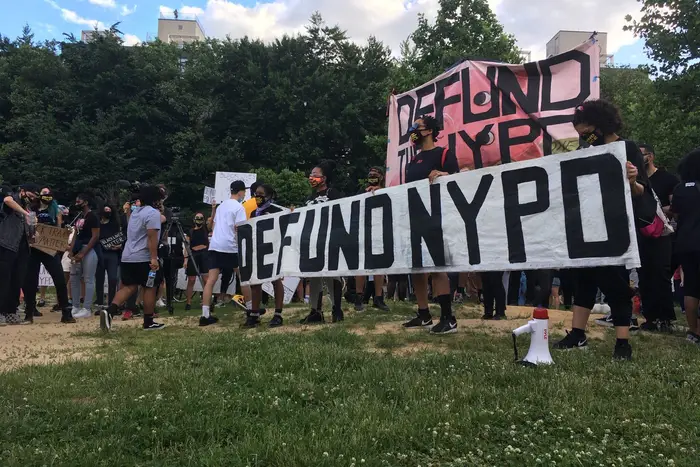 Protesters hold a sign that says "Defund The NYPD" at McCarren Park on Sunday evening.